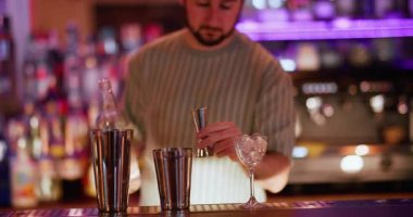 Kokteyl yapımı. Barmen karışımı. Adam alkollü içeceği şişeden metal karıştırıcıya pembe bir içecek püskürterek dolduruyor..