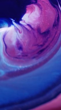 Dikey video. Sıvı lekeler. Akışkan sanat. Odaklanmamış kırmızı, mavi renkli, emaye rengi, soyut kozmetik arka planda suya jel boya damlatıyor..