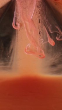 Dikey video. Haze düşüşü. Duman akışı. Suda yüzen parlak turuncu mürekkep peçesi. Siyah parlayan piramit üzerinde kayan parlak boya soyut arkaplan bulanıklığı.