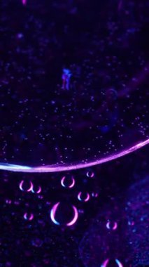 Dikey video. Emülsiyon esansı. Jel serumu. Bulanık mavi neon rengi yağ yuvarlak baloncukları koyu soyut sanat ışığı arka planında hareket ediyor.