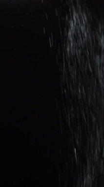 Dikey video. Su çiselemesi. Hafif kar. Odaklanmamış beyaz parçacıklar koyu siyah soyut sanat arka planında yüzen nemli don dokusunu parlatır.