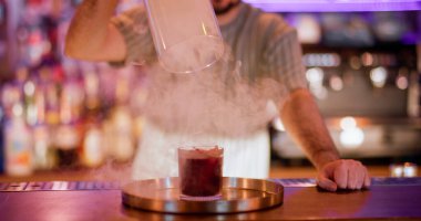 Barmen gösterisi. İçki sunumu. Erkek barmen dumanlı kırmızı alkollü kokteylden cam kaput kaldırıyor. Güzel bir buhar barı tekniği..