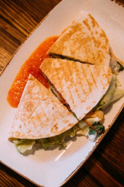 Tortilla yemeği dilimlenmiş. Burrito servis edildi. Kızarmış lahana ile doldurulmuş ekmek. Bulaşık masasında kırmızı baharatlı soslu sıcak yemek..