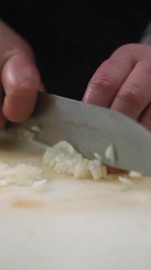 Dikey video. Mutfak kesimi. Baharatlı malzeme. Eller beyaz soğan doğruyor. Şef keskin profesyonel bıçakla küçük parçalar halinde vejetaryen yemeği doğruyor..