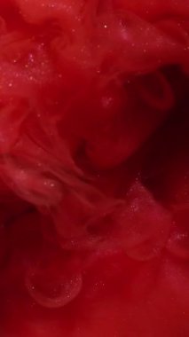 Dikey video. Duman dalgası. Sanat sıvısı. Siyah su yüzeyinde kırmızı parıldayan boya karışımı patlaması. Soyut duman girdabı dağılmış arka plan.