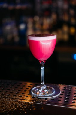 Kokteyl camı. Alkolik içki. Metal bar tezgahında servis edilen pembe likör. Lokantada zarif cam içecekler sunumu.