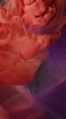 Dikey video. Duman patlaması. Puf boyası. Cam piramidin üzerindeki turuncu püskürtme bulutu mor simli jel soyut su çözünmüş arka plan.