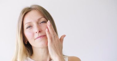 Güzellik bakımı. Kozmetik rutini. Beyaz fotokopi arkaplanındaki makyajdan önce kadın cildine nemlendirici losyon süren kadın..