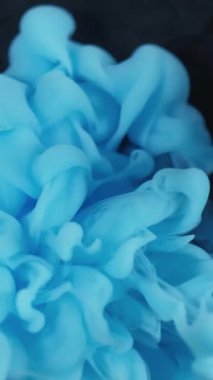 Dikey video. Bulut karışımı. Boya patlamış. Siyah arkaplana yayılmış mavi tüttürme spreyi. Soyut su rengi lekesi patlaması bulanık duvak fantezi sisi.