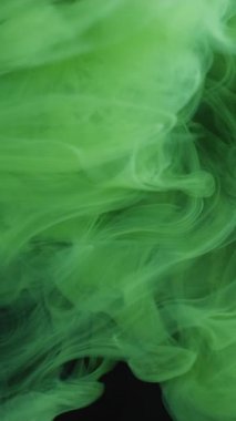 Dikey video. Renk buharı. Sis akışı. Yeşil duman mürekkebi yumuşak akıntı suyu karıştırır. Siyah mistik renk sanatı sis arkaplanını dağıttı.