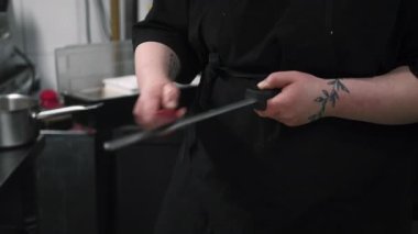 Keskinleştirme bıçağı. Mutfak aletleri hazırlanıyor. Siyah üniformalı şef çelik çubuk kullanıyor. Profesyonel yemek pişirme aleti..