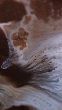 Dikey video. Mürekkep dalgası. Sıvı dökülmesi. Soyut zemin üzerinde yüzen sıvıdaki kahverengi renkli kimyasal mermer parçacıkları çözünmüş..