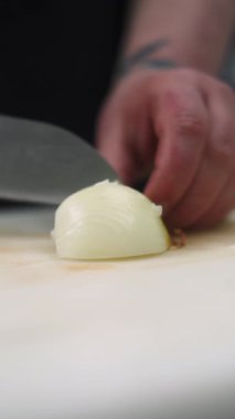 Dikey video. Aşçı kesimi. Malzeme doğruyorum. Mutfak tahtasındaki bıçaklı beyaz soğanı ustalıkla hazırlıyorum. Çiğ taze vejetaryen mutfağı..