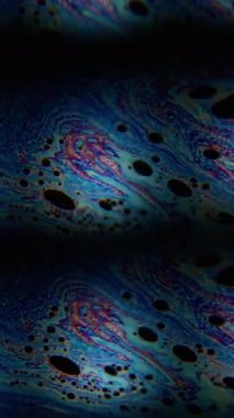 Dikey video. Kaleydoskop etkisi. Benzin döküldü. Renkli bulanık resim boyası sıvı siyah sıvı üzerinde akıyor. Mercek hareketini klonla soyut arkaplan.