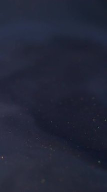 Dikey video. Renk dalgalanması mürekkebi. Su altı dokusu. Bulanık mavi neon parlak su kimyasal parçacıkları soyut koyu siyah arkaplan üzerine dökülüyor.