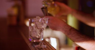 Kokteyl yapımı. Jigger kullanarak. Barmen, soğutulmuş alkolik için sarı sıvı dolduruyor. Metal ölçü kabından cam buz küplerine kadar içki içiyor..