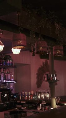 Dikey video. Barın içinde. Restoran ışığı. Barda bardaklarla aydınlatılmış içki şişeleri. Duvarlarda egzotik palmiye yapraklarıyla süslenmiş bir oda..