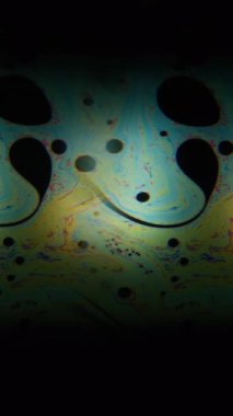 Dikey video. Kaleydoskop etkisi. Benzin döküldü. Renkli bulanık resim boyası sıvı siyah sıvı üzerinde akıyor. Mercek hareketini klonla soyut arkaplan.