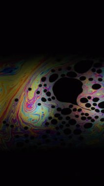 Dikey video. Gökkuşağı küresi. Yağ pigmenti. Odaklanamayan bulanık arkaplanda daire mercek. Soyut yüzen benzin neon mürekkep harman sıvısı siyah.