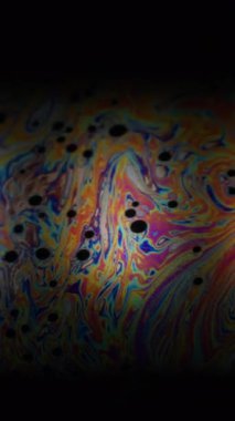 Dikey video. Psikedelik baloncuk. Girdap sabunu. Renkli benzinli su. Siyah arkaplanda resim sıvısı bulanık neon boya dairesi küresi.