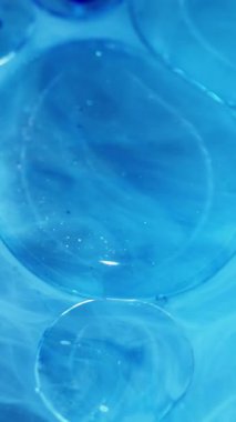 Dikey video. Yağlı mermiler. Sıvı jel. Odaklanmamış mavi renk moleküler boya lekeli kimyasal su akışı soyut sanat akrilik arka planda yayılıyor..