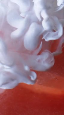 Dikey video. Pürüzsüz sis. Boya spreyi. Beyaz mürekkep dumanı portakal rengi pırıltılı elmasa damlıyor. Soyut bulanık arkaplan dökülüyor.