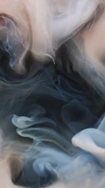 Dikey video. Renk buharı. Sis akışı. Bej mavisi gri duman mürekkebi yumuşak akım suyu karışımı döker. Siyah mistik renk sanatı sis arkaplanını dağıttı.