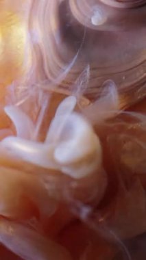 Dikey video. Parıldayan sıvı. Sanat buharı. Beyaz bej rengi altın peçeli dalga toz mat üzerine boya döküyor kristal şeftali soyutlanmış arkaplan.