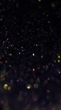 Dikey video. Bulanık parıltılar. Bokeh ışığı. Soyut sanatın koyu siyah zemininde sönük sarı altın mavisi parıltı.