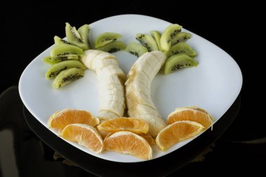 izole et. Siyah arka plan. muz, kivi ve turuncu bir plaka üzerinde kompozisyon