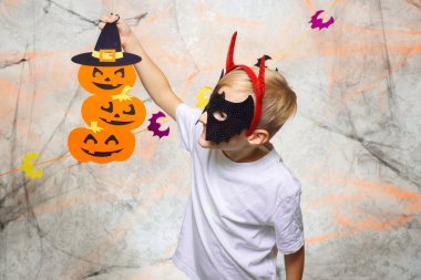 Maskeli ve boynuzlu bir çocuk Cadılar Bayramı balkabağıyla oynuyor.