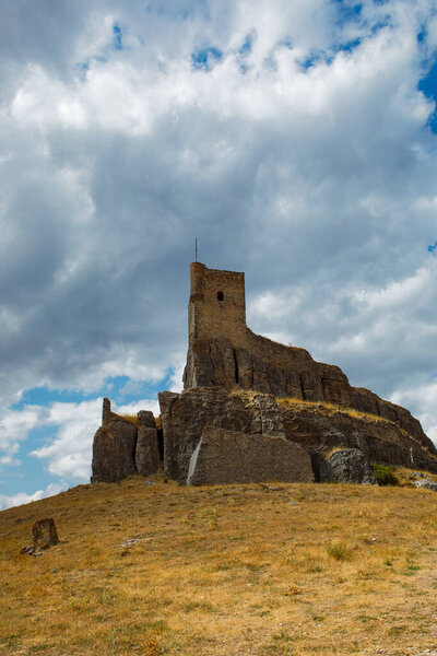 Atienza castle stands majestically atop a rocky hill in Guadalajara, Spain, showcasing its storied past against a backdrop of dramatic clouds. The landscape is dry and rugged.