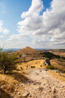 İspanya, Atienza, Guadalajara 'yı çevreleyen kayan tepelerin manzarası, açık hava keşfi ve fotoğrafçılık için mükemmel, parlak bir gökyüzü altında antik kalıntıları ve çimenli araziyi gösteriyor..