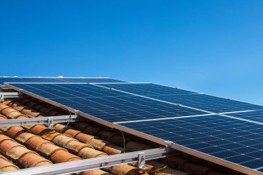 Güneş panelleri açık mavi bir gökyüzünün altında fayanslı bir çatıya monte edilir. Kurulumda konut kullanımı için çevre dostu enerji üretimi sergileniyor.