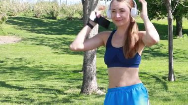 Dışarıda ayakta dururken kulaklıkla müzik çalan kadın koşucunun yavaş çekimleri. Yüksek kalite 4k görüntü