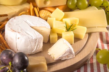 Üzerinde çeşitli peynirler ahşap tahta plaka yuvarlak. Camembert peyniri, peynir meşe, sert peynir dilimleri, ceviz, üzüm, kraker, ekmek, incir kabuğu rendesi