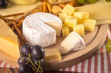 Üzerinde çeşitli peynirler ahşap tahta plaka yuvarlak. Camembert peyniri, peynir meşe, sert peynir dilimleri, ceviz, üzüm, kraker, ekmek, incir kabuğu rendesi