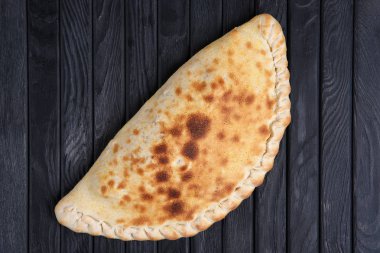 Taze pişmiş pizza calzone koyu ahşap tablo, üstten görünüm.