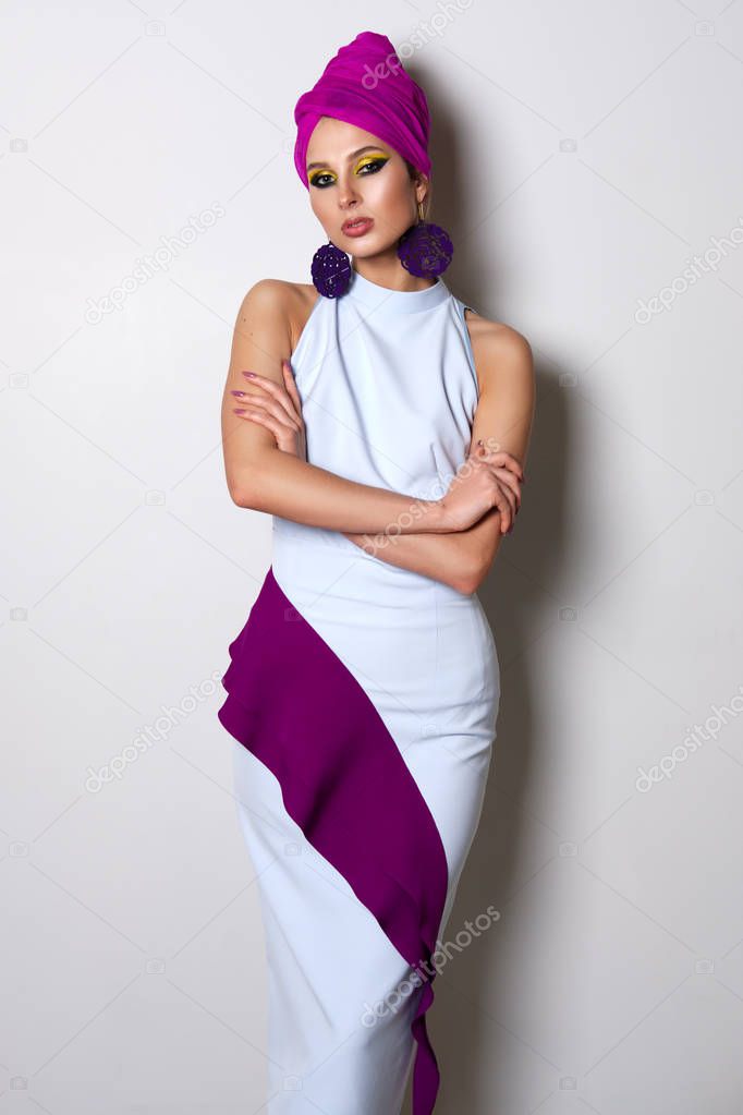 Portrait of beautiful fashion model in fitted dress and turban on head. Bright makeup and big earrings