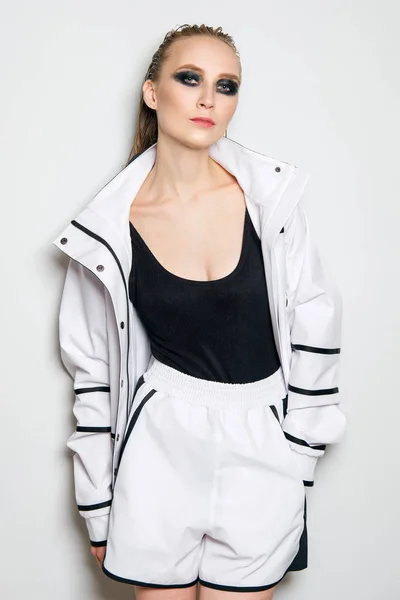 Portrait of fashion model in white sports suit. Girl in unzipped jacket, sleeveless t-shirt and wide shorts - sportive outfit.