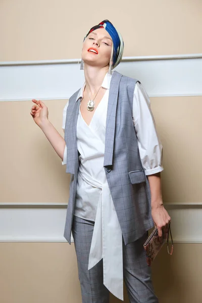 Beautiful fashion model in sleeveless jacket, long asymmetric  shirt, pants and turban posing