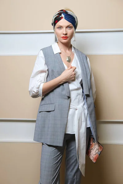 Beautiful fashion model in sleeveless jacket, long asymmetric  shirt, pants and turban posing
