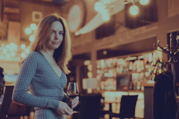 Photo with shallow depth of field, toned and stylized as a film of a cute girl with glass of red wine in her hand in a bar