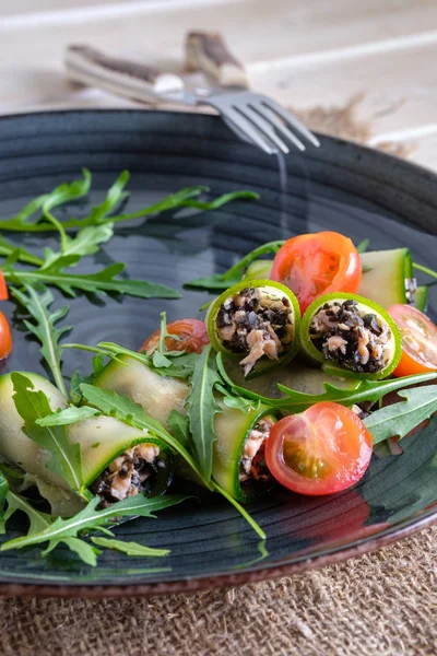Chopped smoked salmon and black olives rolled in cucumber decorated with tomato and arugula — Stock Photo, Image