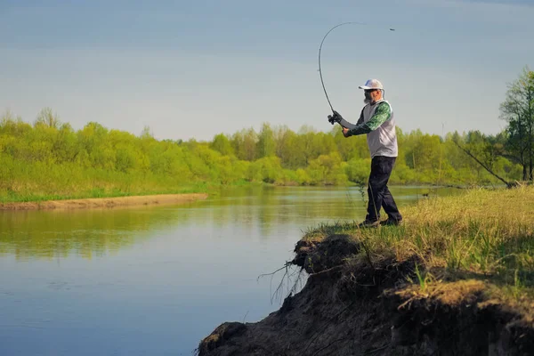 Hombre pez con spinning en la orilla del río, lanzando señuelo. Actividad al aire libre. Foto con profundidad de campo poco profunda tomada en abertura abierta amplia . —  Fotos de Stock
