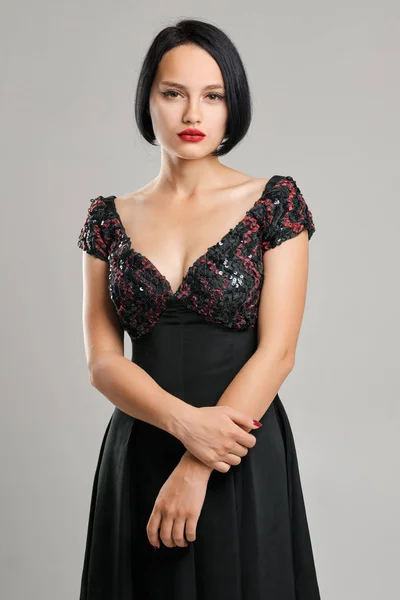 Serious lady with short dark hair and red lips looking straight slightly arrogant.