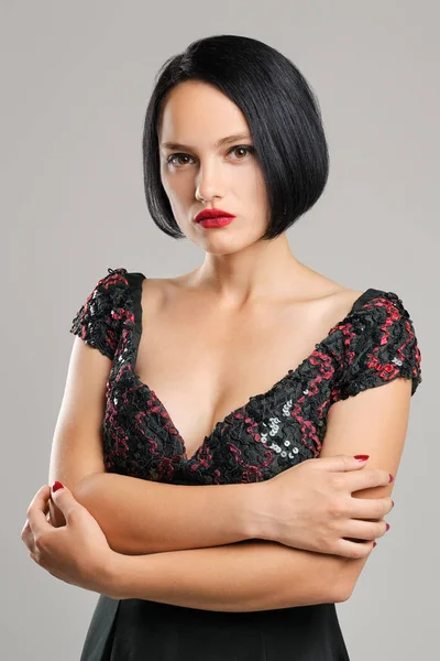 Serious lady with short dark hair and red lips looking straight slightly arrogant.