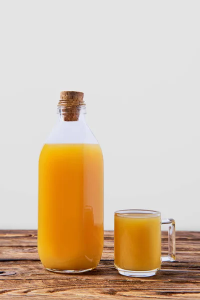 Sumo de laranja fresco em garrafa e caneca na mesa de madeira — Fotografia de Stock