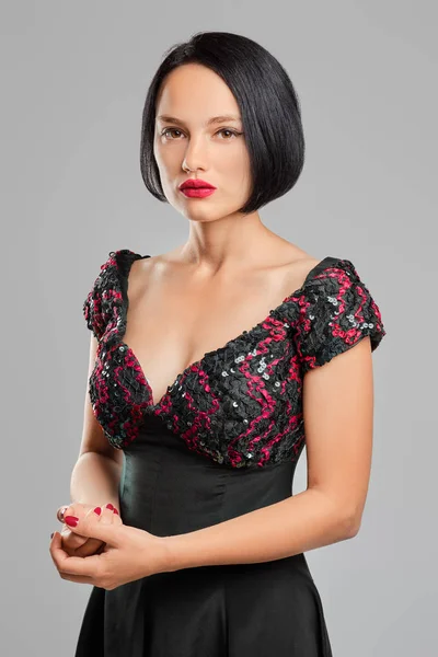 Serious lady with short dark hair and red lips posing in studio