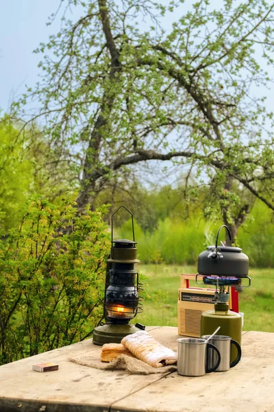 Snack outdoor in summer evening. Camping kettle, cups and biscuit on rustic table.